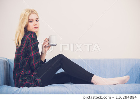 Teenage woman sitting on sofa with mug 116294884