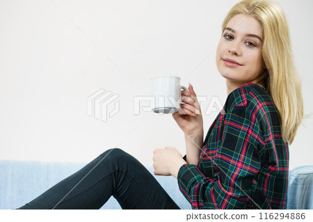Teenage woman sitting on sofa with mug 116294886