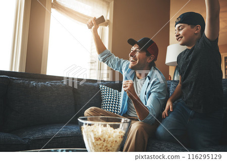 Television, child and man with celebration on sofa for streaming, network and watching together. Dad, son and popcorn with tv remote at home for success, bonding and live broadcast of sports match Television, child and man with celebration on sofa for streaming, network and watching together. Dad, son and popcorn with tv remote at home for success, bonding and live broadcast of sports match 116295129