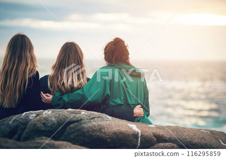 Friends, beach and sunset of people sitting on rock for bonding, back view and embrace in Ireland. Vacation, group and relax for fun day by ocean, nature or contemplation in outdoors for togetherness Friends, beach and sunset of people sitting on rock for bonding, back view and embrace in Ireland. Vacation, group and relax for fun day by ocean, nature or contemplation in outdoors for togetherness 116295859