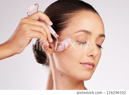 Skincare, roller and woman in studio with eyes closed for facial treatment, massage on white background. Stone, gua sha and hand of model with tool for rose quartz, dermatology or lymph cleaning Skincare, roller and woman in studio with eyes closed for facial treatment, massage on white background. Stone, gua sha and hand of model with tool for rose quartz, dermatology or lymph cleaning 116296102