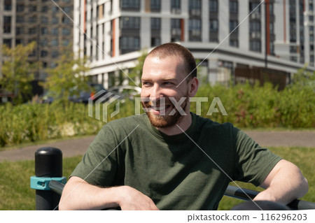 Portrait of happy caucasian handsome beard man wearing military color t-shirt. Athlete man on outdoor sports ground. Courtyard. Outdoors. Summer. 116296203