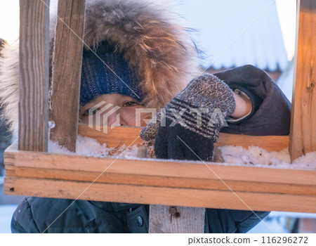 Close-up of an adorable child, boy feeding birds on a cold winter day, pouring grain into a feeder. A child helps birds in winter. Winter activities for children. 116296272