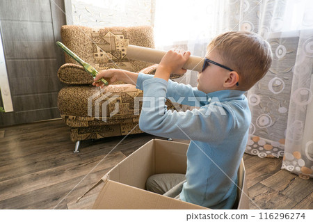 Playful cheerful child, boy looking into a cardboard tube, sitting in a box. Playful cheerful child, boy looking into a cardboard tube, sitting in a box. 116296274
