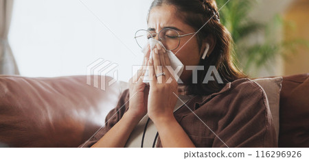 Sick, tissue and woman on sofa with in home with earbuds listening to music, podcast or radio. Illness, living room and female person blow nose with flu, cold or allergies streaming playlist at house 116296926