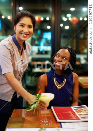 Customer, portrait and waiter with cocktail in restaurant, diner and consumer service in bistro. Black woman, drink and female server with smile for assistance, bartender and hospitality or dining Customer, portrait and waiter with cocktail in restaurant, diner and consumer service in bistro. Black woman, drink and female server with smile for assistance, bartender and hospitality or dining 116297718