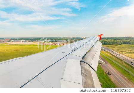 View of airplane wing, blue skies and green land during landing. Airplane window view. 116297892