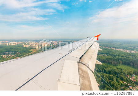 View of airplane wing, blue skies and green land during landing. Airplane window view. 116297893