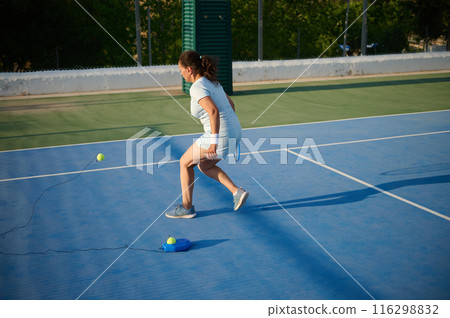 Woman practicing tennis on court with ball trainer under sunlight Woman practicing tennis on court with ball trainer under sunlight 116298832