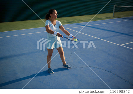 Female tennis player practicing on outdoor blue court Female tennis player practicing on outdoor blue court 116298842