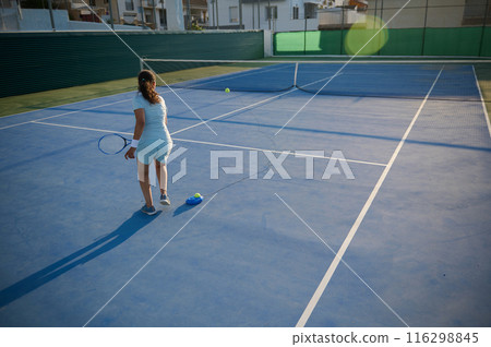 Woman playing tennis on an outdoor blue court at sunset 116298845