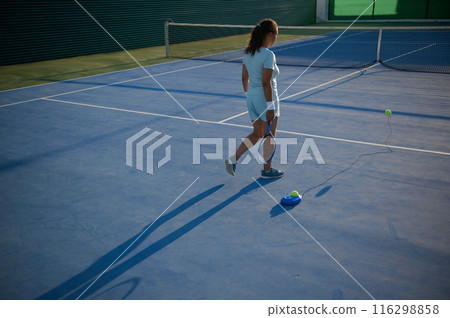 Woman practicing tennis alone on outdoor court under sunlight Woman practicing tennis alone on outdoor court under sunlight 116298858