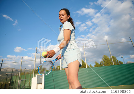 Woman preparing to serve tennis ball on outdoor court 116298865
