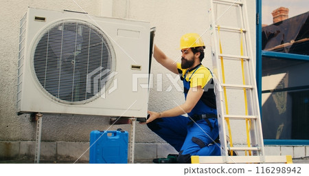 Professional worker starting work on malfunctioning air conditioner, using power drill to take apart condenser side coil panel. Capable electrician dismantling hvac system to check for faulty wires Professional worker starting work on malfunctioning air conditioner, using power drill to take apart condenser side coil panel. Capable electrician dismantling hvac system to check for faulty wires 116298942