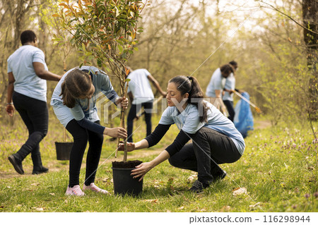 Mother and daughter preparing to plant a tree in the woods, volunteering to help with nature conservation and reforestation. Activists offering service to fight for environmental protection. Mother and daughter preparing to plant a tree in the woods, volunteering to help with nature conservation and reforestation. Activists offering service to fight for environmental protection. 116298944