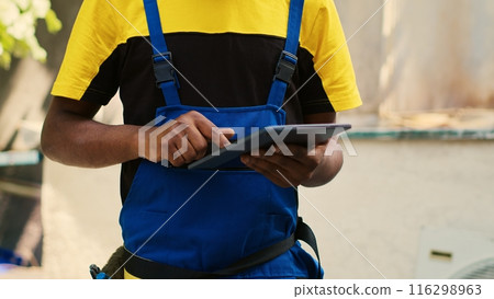 Revealing portrait shot of smiling qualified electrician checking freon levels in air conditioner while using manifold indicators to accurately measure the pressure in HVAC system Revealing portrait shot of smiling qualified electrician checking freon levels in air conditioner while using manifold indicators to accurately measure the pressure in HVAC system 116298963