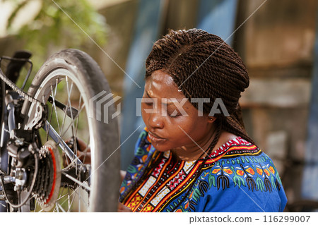 Dedicated sports-loving black woman meticulously inspects her bike chain using professional tool. Young african american lady adjusting and securing modern bicycle parts as summer maintenance activity Dedicated sports-loving black woman meticulously inspects her bike chain using professional tool. Young african american lady adjusting and securing modern bicycle parts as summer maintenance activity 116299007