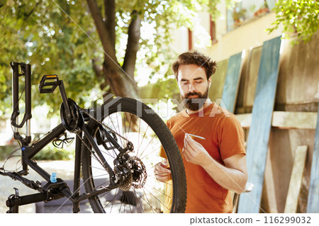 Determined male cyclist expertly using specialized equipment to adjust bike components in home yard. Young sporty caucasian man grasping torx wrench for repairing modern bicycle. 116299032