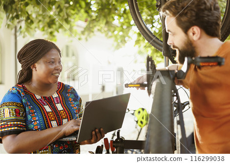 Young active vibrant multiethnic couple surfing the internet for bicycle gear maintenance. Sport enthusiasts boyfriend and girlfriend servicing bike pedals while using laptop for yearly summer cycling Young active vibrant multiethnic couple surfing the internet for bicycle gear maintenance. Sport enthusiasts boyfriend and girlfriend servicing bike pedals while using laptop for yearly summer cycling 116299038