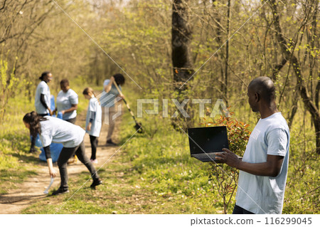African american activist checks isolated mockup on laptop, participates in collecting rubbish from the forest area. Environmental volunteer works to protect the ecosystem, community outreach. African american activist checks isolated mockup on laptop, participates in collecting rubbish from the forest area. Environmental volunteer works to protect the ecosystem, community outreach. 116299045