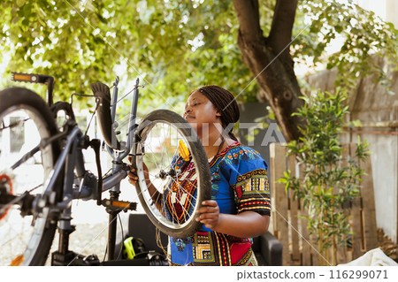 Young athletic african american woman mending modern bicycle professional work tool. Active and determined female cyclist confidently reattaching bike wheel rubber and inspecting tire for outdoor 116299071
