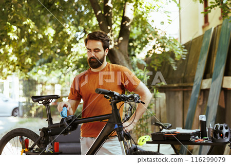 Healthy committed caucasian man clamping bike frame to repair-stand for safe outdoor maintenance. Sports-loving male cyclist realigning and adjusting bicycle for servicing in yard. 116299079