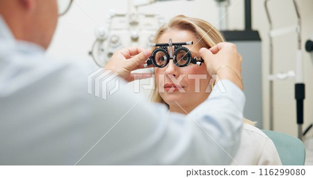 Doctor, ophthalmologist and woman with test frame for eye health, consultation and exam in clinic. Optometry, trail and patient on lens for vision check, wellness and glasses for eyesight correction 116299080