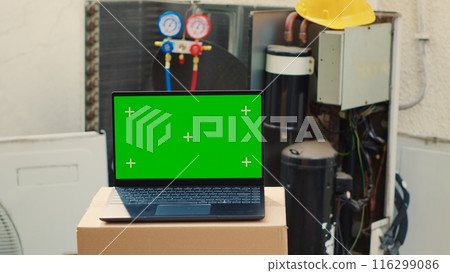 Green screen laptop in front of malfunctioning outdoor HVAC system. Mock up chroma key gadget display next to faulty condenser in need of professional refurbishing by specialists Green screen laptop in front of malfunctioning outdoor HVAC system. Mock up chroma key gadget display next to faulty condenser in need of professional refurbishing by specialists 116299086