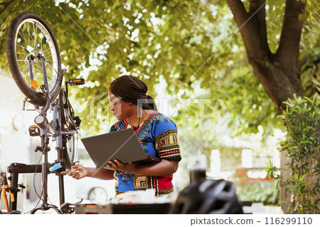 A healthy and lively african american fermale looking for bike gear maintenance for summer activities on internet. Sporty black woman searches for instructions on laptop to repair bicycle. 116299110