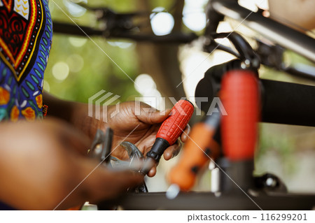 Close-up shot of african american hands grasping bicycle tools from professional toolbox for maintenance and repairs. Detailed image of individual adjusting specialized equipments. Close-up shot of african american hands grasping bicycle tools from professional toolbox for maintenance and repairs. Detailed image of individual adjusting specialized equipments. 116299201