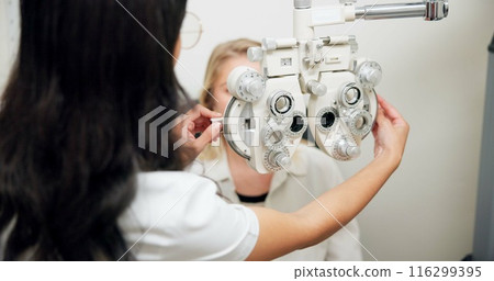 Doctor, optometry and woman on phoropter for eye care, consultation or health exam in clinic. Ophthalmologist, test or patient on lens machine tool for vision check, wellness and eyesight correction 116299395