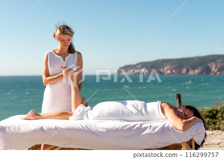 Female masseur massages client's legs on ocean Female masseur massages client's legs on ocean 116299757