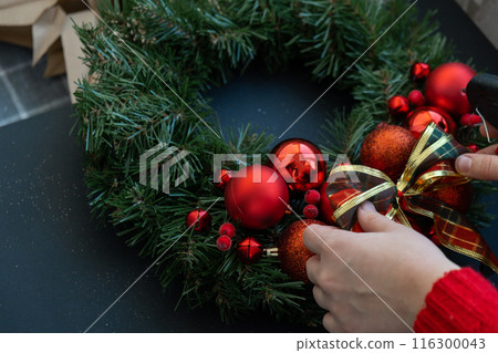 Woman tying decorative ribbon Step by step instruction of making handmade Christmas wreath made of festive decorations in red color. Female hands creating craft homemade decor. New year celebration Woman tying decorative ribbon Step by step instruction of making handmade Christmas wreath made of festive decorations in red color. Female hands creating craft homemade decor. New year celebration 116300043