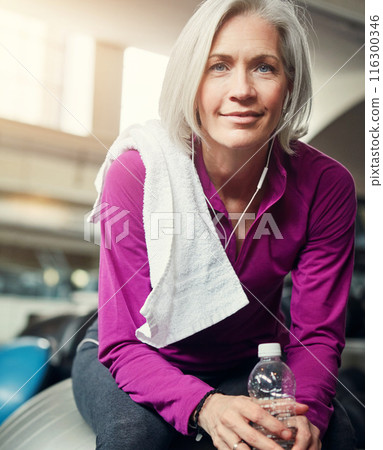 Woman, portrait and bottle in gym on ball for break, hydration and tired from workout for wellness. Mature person, water and relax with pride, fatigue and smile with towel at training for fitness 116300346