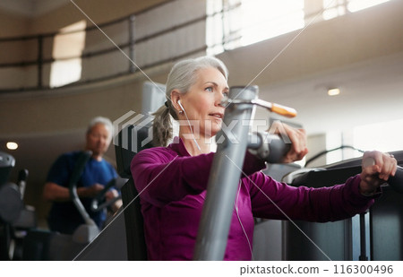 Mature woman, chest press and music with machine for fitness, workout or indoor exercise at gym. Active female person with earphones on equipment for strength, muscle or wellness at health club 116300496