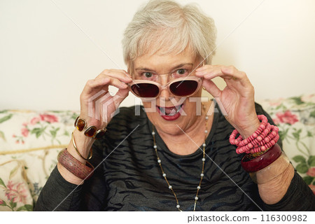 Sunglasses, portrait and senior woman on sofa for fun, excited and humor in living room. Elderly person, comedy and designer glasses on couch for style, funny and cool personality in retirement home Sunglasses, portrait and senior woman on sofa for fun, excited and humor in living room. Elderly person, comedy and designer glasses on couch for style, funny and cool personality in retirement home 116300982