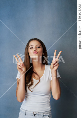 Peace sign, kiss and portrait of woman in studio for romance, affection and gratitude. Beauty, confidence and face of person with flirting emoji, positive hand gesture and love on blue background 116301288