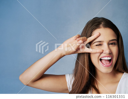 Happy woman, portrait and face with peace sign for friendly, funky or positive attitude on a blue studio background. Female person, brunette or young model with smile or emoji for cool, fun or humor Happy woman, portrait and face with peace sign for friendly, funky or positive attitude on a blue studio background. Female person, brunette or young model with smile or emoji for cool, fun or humor 116301331