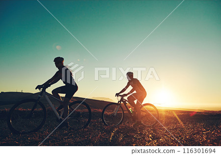 Sunset, silhouette and people on bicycle with fitness, race and exercise in nature together. Cycling, adventure and friends with mountain bike in evening for outdoor workout, blue sky and grass path Sunset, silhouette and people on bicycle with fitness, race and exercise in nature together. Cycling, adventure and friends with mountain bike in evening for outdoor workout, blue sky and grass path 116301694