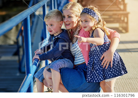 Mother, children and together outdoor for adventure, holiday and love by water or pier. Family, woman and kids on vacation in California with happiness, relationship and pointing at ocean on jetty 116301796