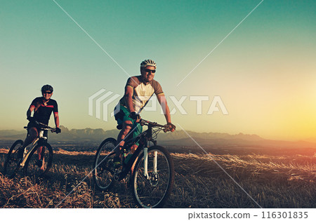 Sunset, mountain and people in bicycle race with helmet, exercise and adventure trail in nature together. Cycling, fitness and friends on bike in evening for outdoor workout, health and wellness 116301835