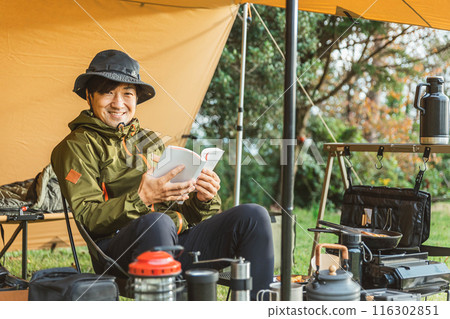 Male camper solo camping at autumn/winter campsite (reading a book) 116302851
