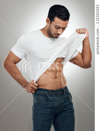 Man, t shirt and undress in studio for fitness, wellness and strong abs muscle on gray background. Male person, clothes and take off for health, bodybuilder and proud of body or workout results Man, t shirt and undress in studio for fitness, wellness and strong abs muscle on gray background. Male person, clothes and take off for health, bodybuilder and proud of body or workout results 116302881