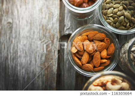 Bowls, almond and nuts on table, above and mock up space for nutrition, health and promotion for wellness. Cashew, hazelnut and pumpkin seeds in glass container for meal prep with food at apartment 116303664