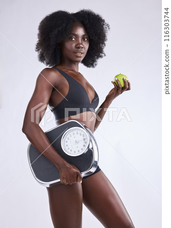 Fitness, scale and black woman portrait with apple in studio for wellness, gut health and diet, detox or balance on white background. Body, care and model with organic, fruit or weight loss progress Fitness, scale and black woman portrait with apple in studio for wellness, gut health and diet, detox or balance on white background. Body, care and model with organic, fruit or weight loss progress 116303744