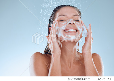 Woman, facial and soap for skincare hygiene with foam, wash or clean against blue studio background. Happy, splash and model person for body wellness, cosmetics or healthy skin treatment in water 116304034