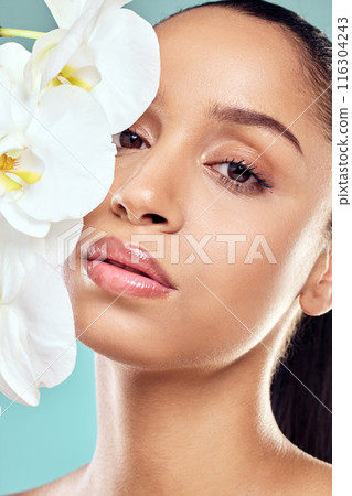 Woman, flowers and portrait in studio with skincare, wellness and organic care on blue background. Natural beauty, female person and orchids for feminine hygiene or purity, growth and delicate skin 116304243