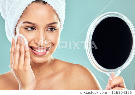 Woman, cotton pad and towel with mirror in studio for wellness, health and face products. Female person, skincare and cosmetic for results, pride and dermatology for glowing skin in blue background Woman, cotton pad and towel with mirror in studio for wellness, health and face products. Female person, skincare and cosmetic for results, pride and dermatology for glowing skin in blue background 116304336