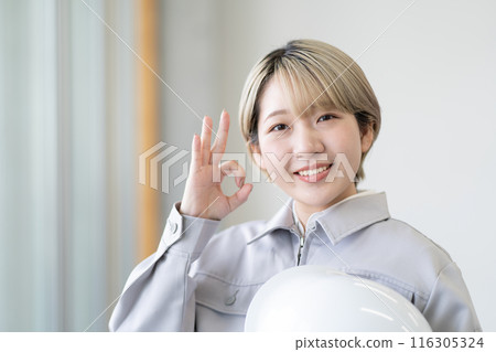 A young woman with short blonde hair wearing work clothes and holding a helmet (OK, free hair color, work the way you want, work environment) 116305324