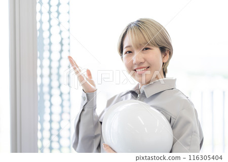 A young woman with short blonde hair wearing work clothes and holding a helmet (OK, free hair color, work the way you want, work environment) 116305404